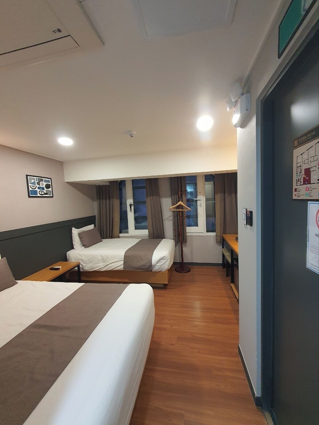 A hotel room with two beds, a desk, a chair, a coat rack, and a window with curtains.