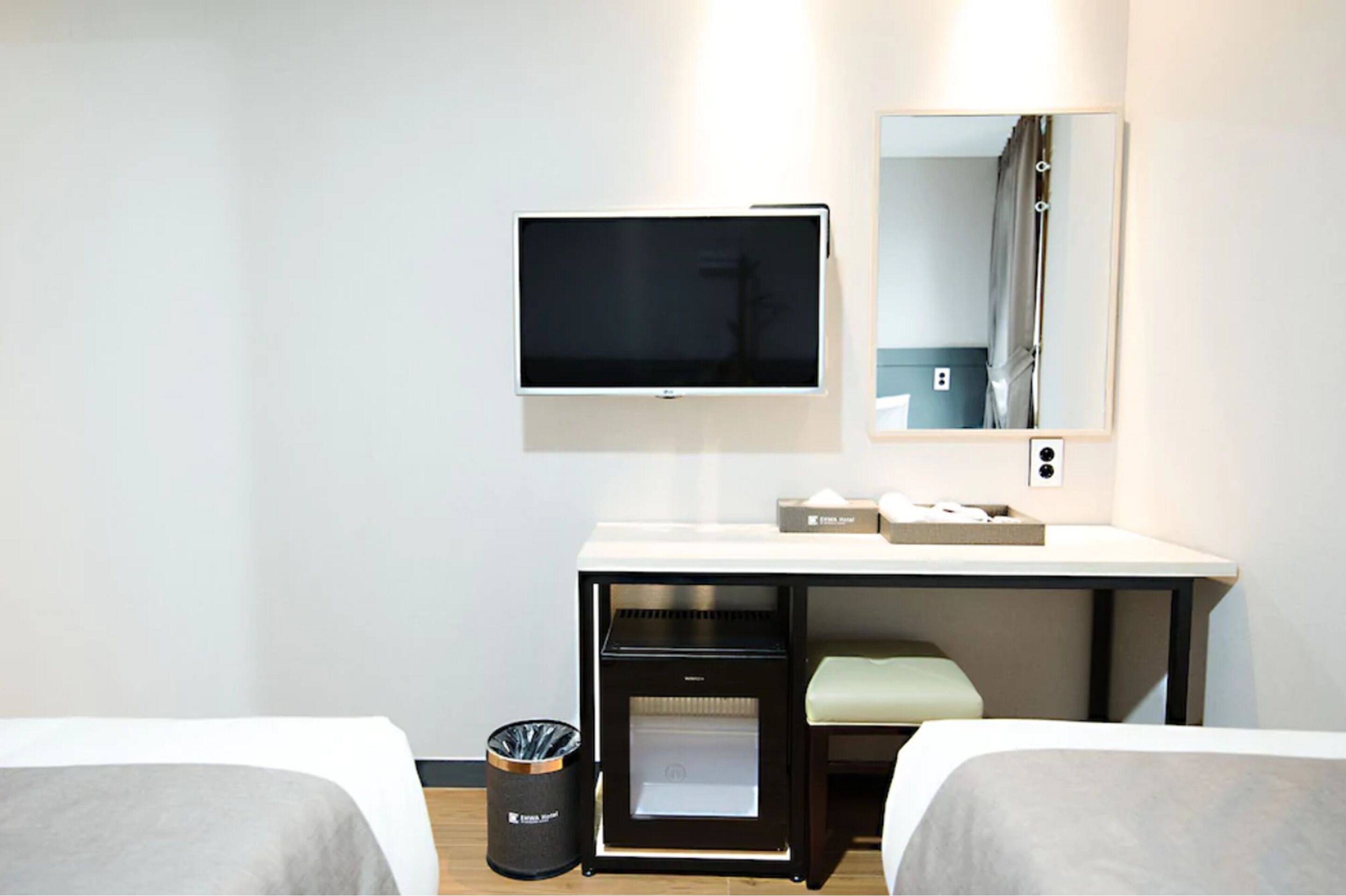 Una habitación de hotel con cama, escritorio con televisor, espejo y cesto de basura.