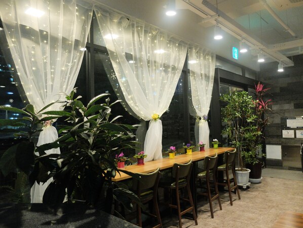 Un comedor con una larga mesa de madera, sillas y plantas en macetas.
