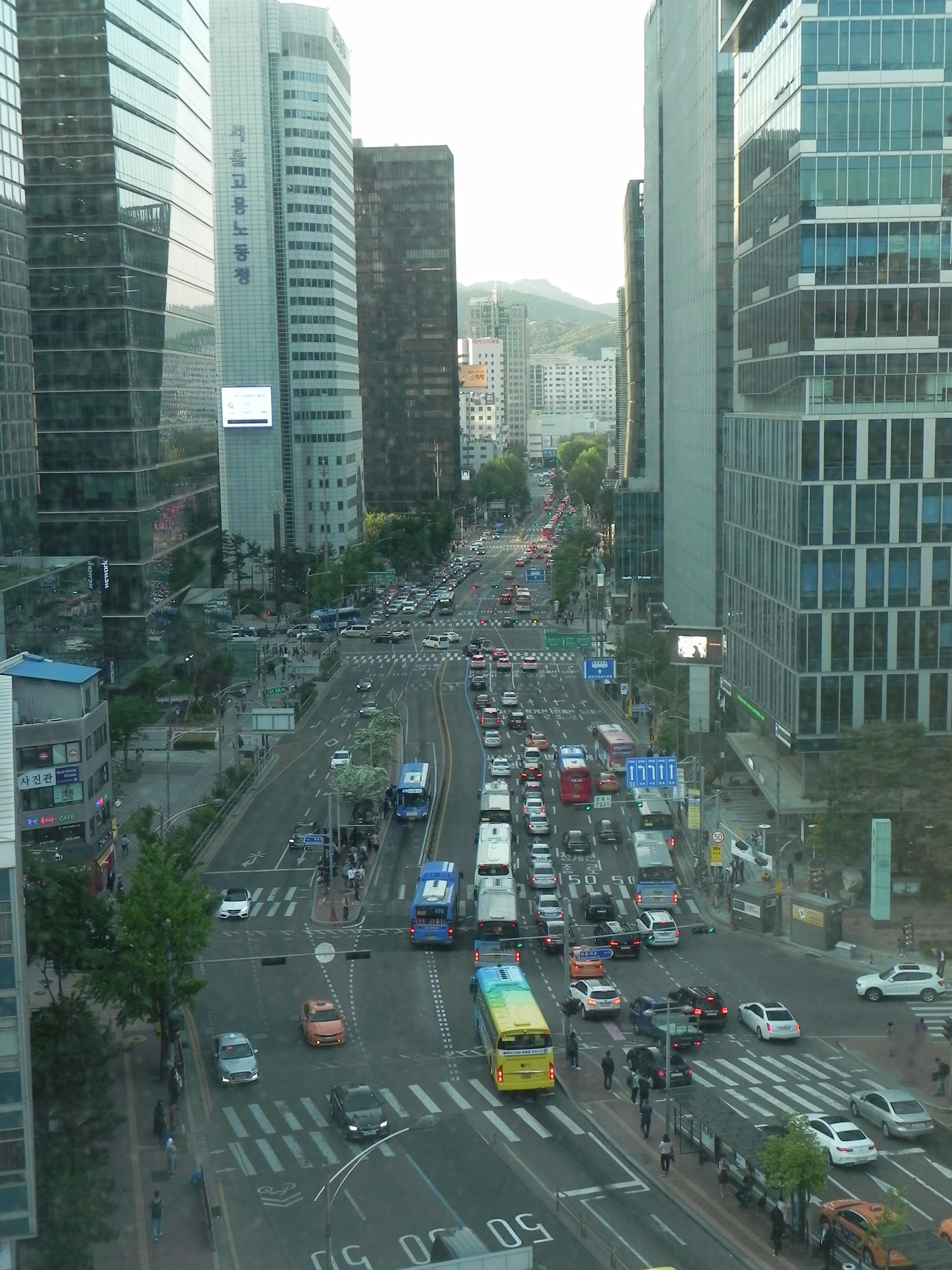A busy urban street with tall buildings, a yellow bus, and various vehicles.