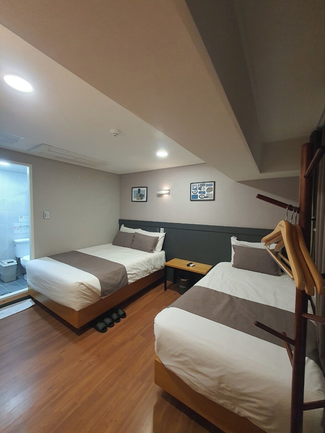 A bedroom with two beds, a wooden floor, a small table, and a wall-mounted light fixture.