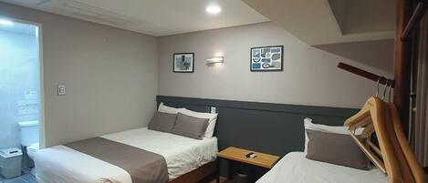 A bedroom with two beds, a wooden floor, a small table, and a wall-mounted light fixture.