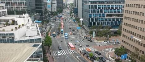 A busy urban street with modern buildings, a pedestrian crossing, and a bus stop.