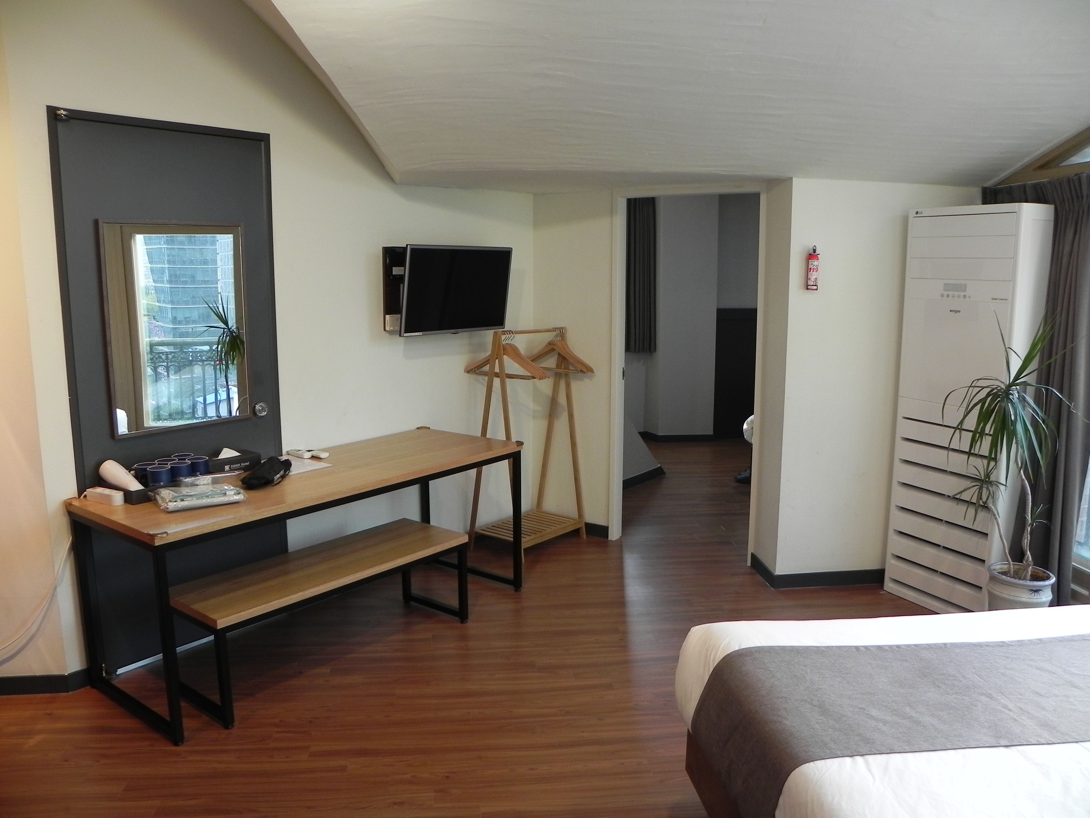 Een hotelkamer met een bed, een bureau, een televisie, een kledingkast en een kamerplant.