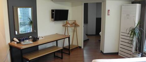 A hotel room with a bed, a desk, a TV, a wardrobe, and a potted plant.