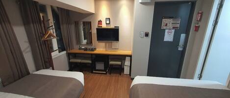 A hotel room with two beds, a desk with a computer, a mirror, and a door with emergency exit signs.