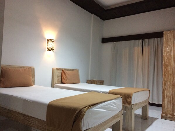 Habitación de hotel con dos camas individuales, cabecera de madera, lámpara de pared y ventana con cortinas.