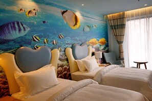 Een hotelkamer met twee bedden, een muurschildering van tropische vissen en uitzicht op de oceaan door het raam.