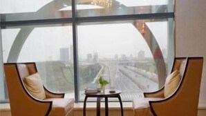 A modern room with two leather armchairs facing a large window overlooking a cityscape. - Metropolo Jinshanzui Village Hotel (Shanghai)