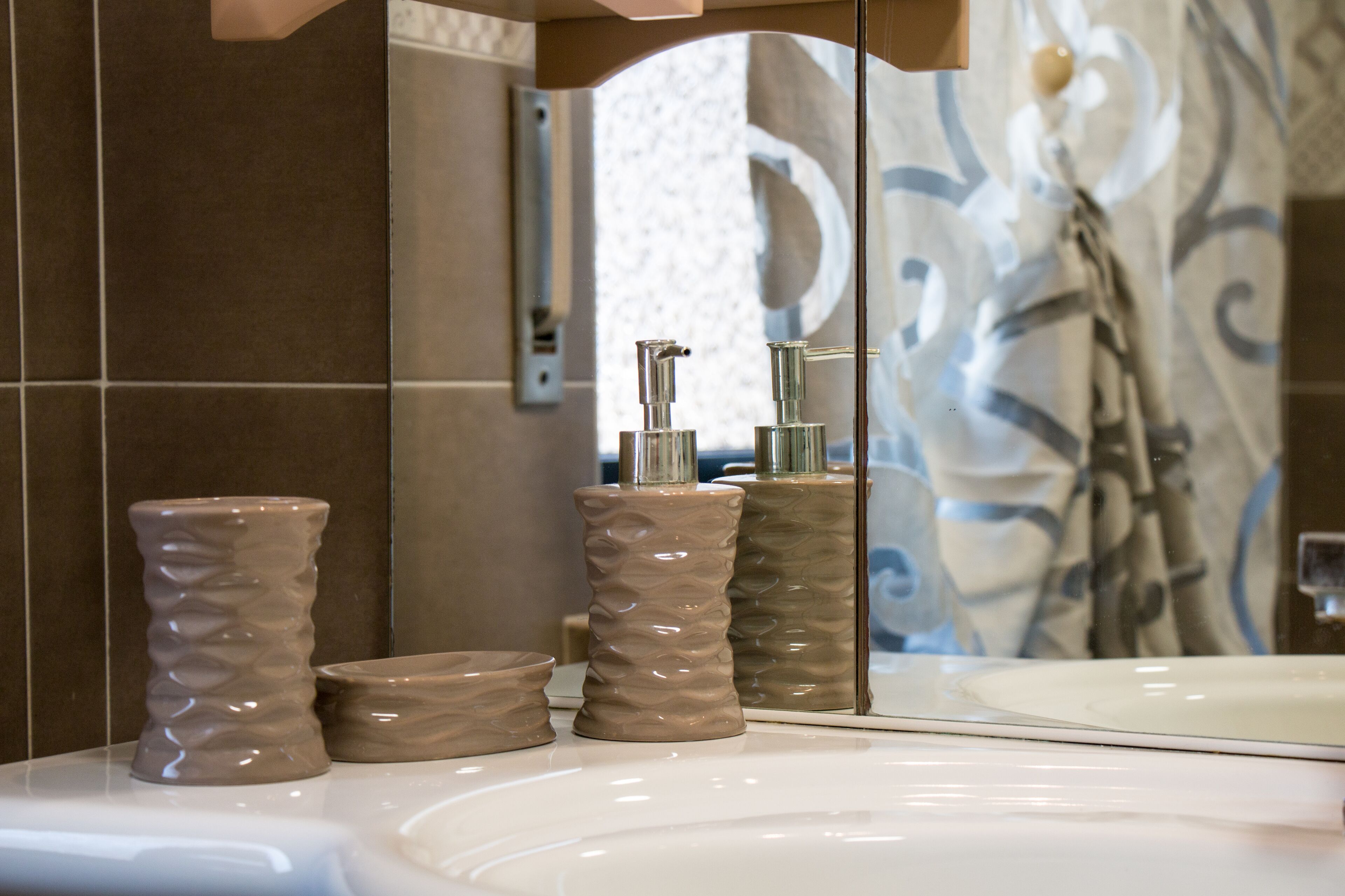 Une salle de bain avec un lavabo blanc, deux distributeurs de savon à texture et un miroir qui reflète un rideau de douche.