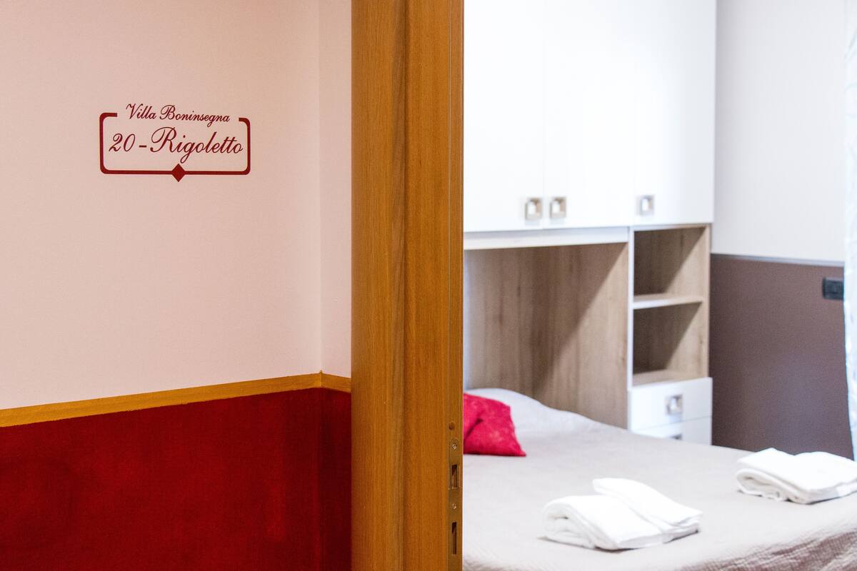 A hotel room with a bed, a wooden wardrobe, and a wall sign indicating the room number and hotel name.