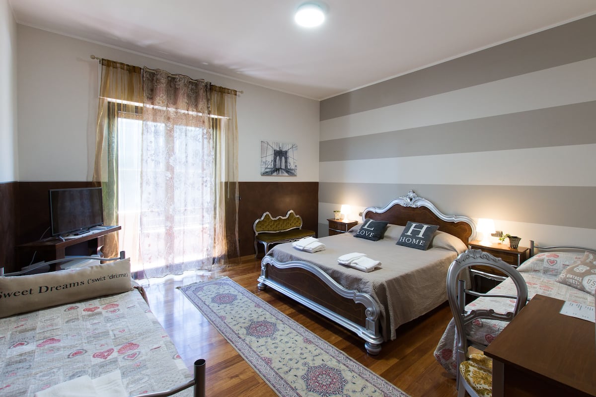 A well-lit bedroom with a large bed, bedside tables, a chair, and a television.