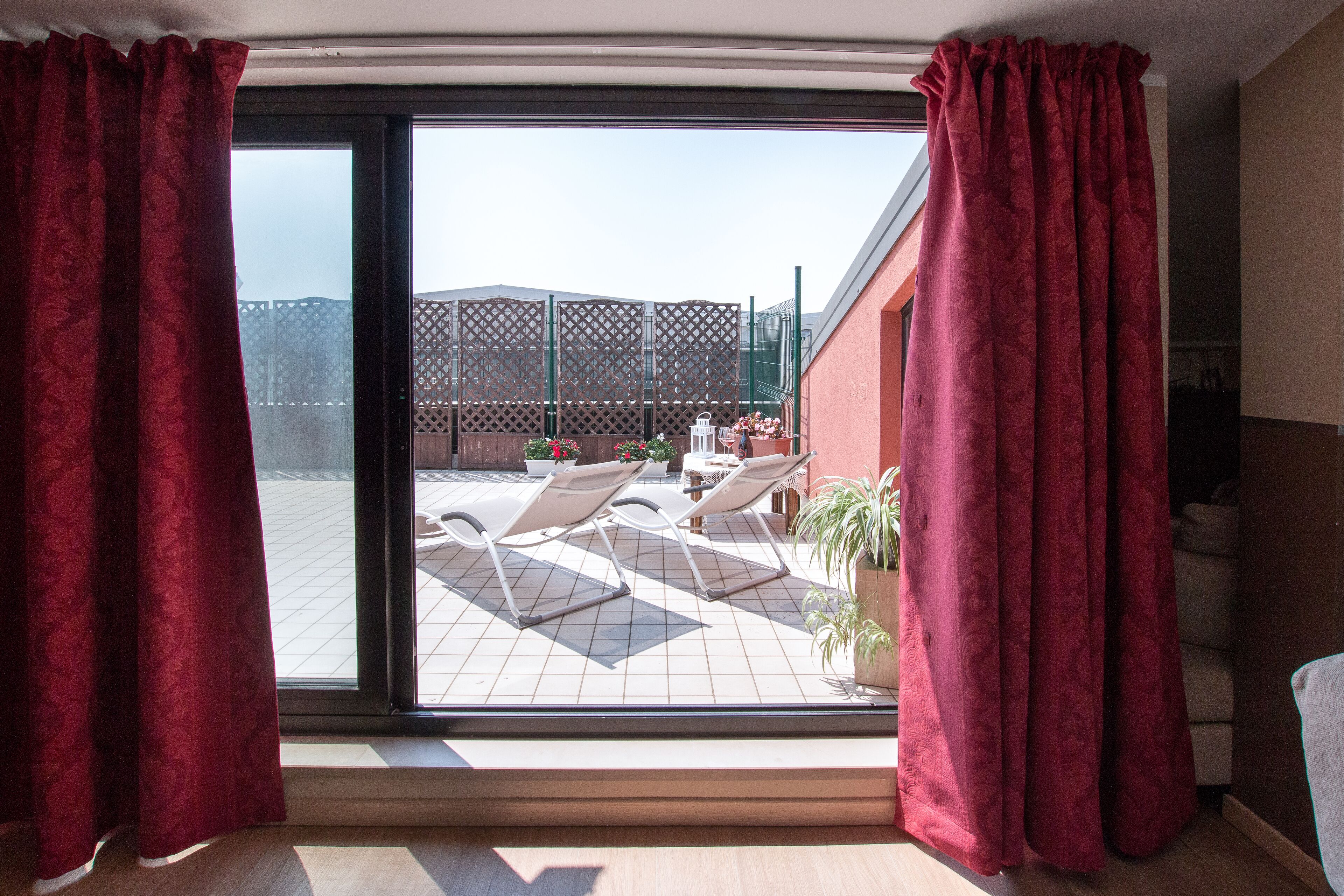 Een kamer met een grote schuifglazen deur die uitkomt op een terras met twee loungestoelen en plantenpotten.