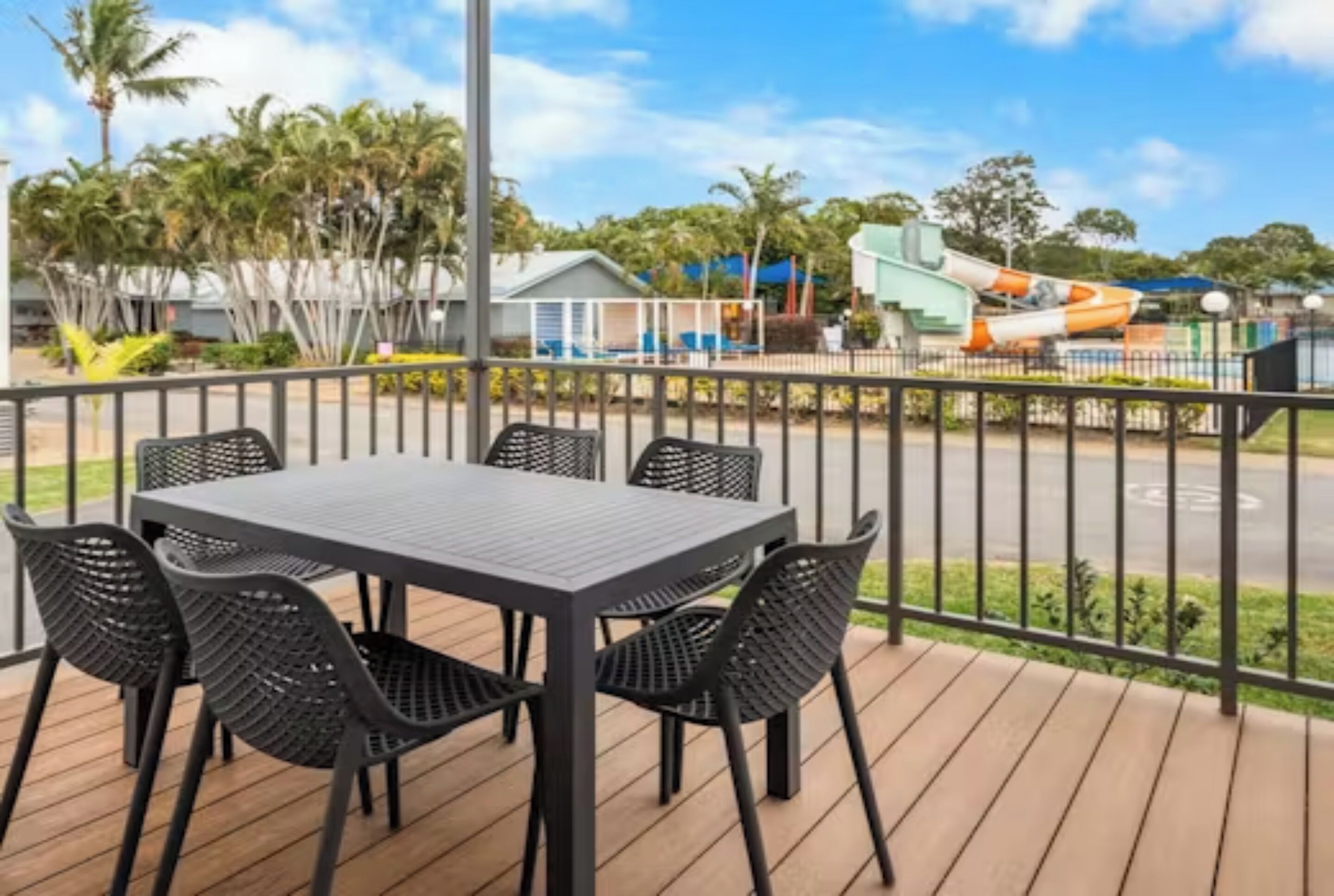 An outdoor patio with a table and chairs, a railing, and a view of a water park in the background.