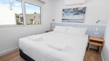 A bedroom with a bed, a nightstand, a window, and a painting on the wall.