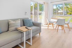 A modern living room with a sofa, a small table, and a dining area with chairs. - Discovery Parks - Coolwaters Yeppoon (Kinka Beach)