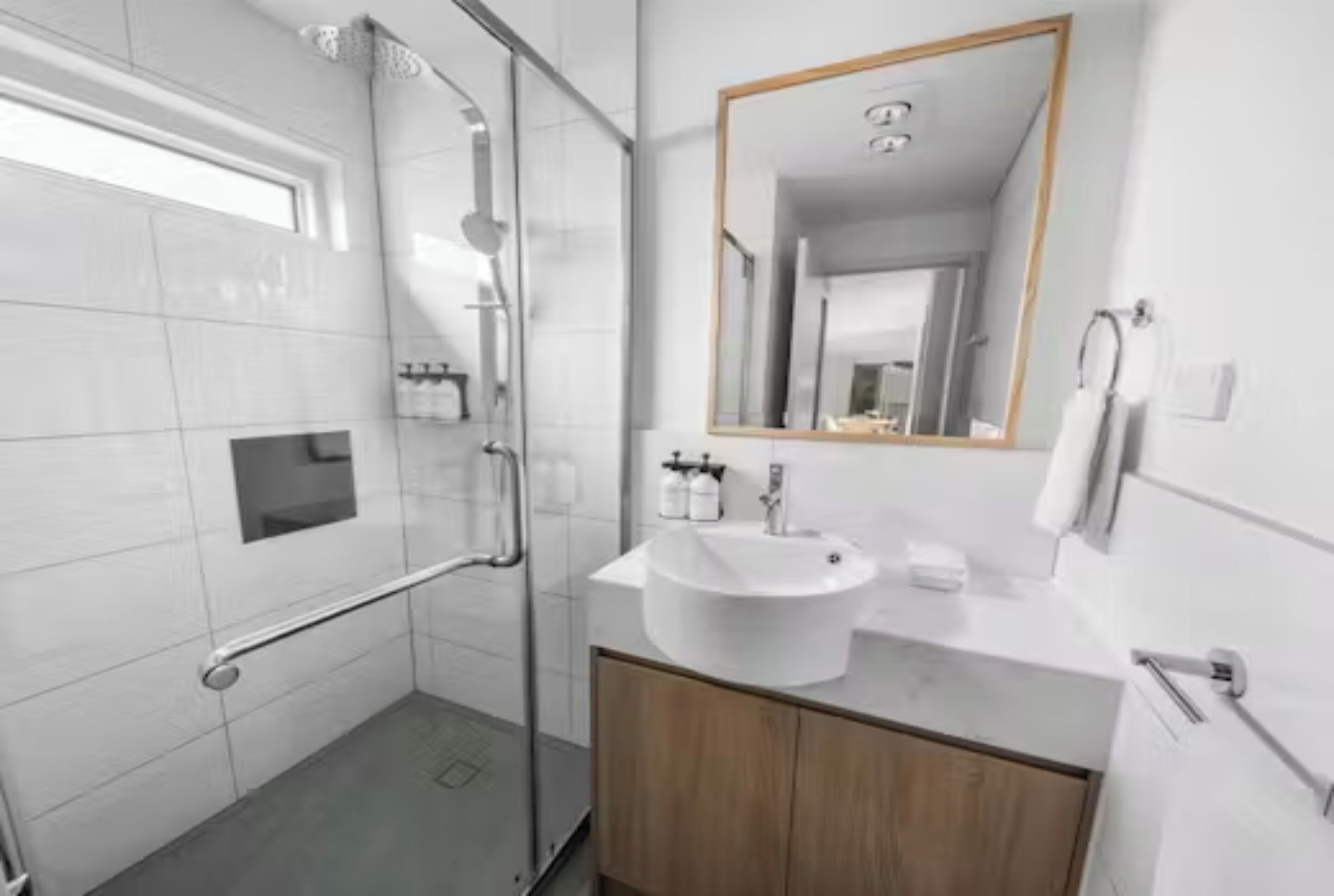 A modern bathroom with a glass shower enclosure, a white sink, and a wooden cabinet.