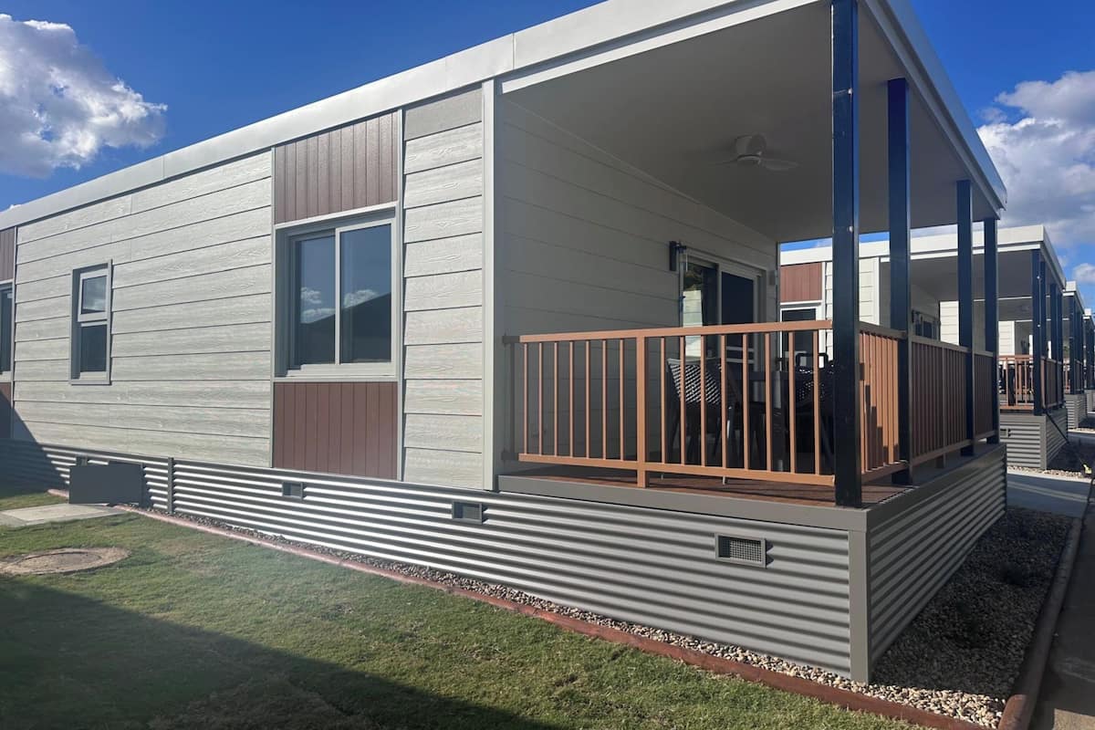 A modern mobile home with a covered porch, large windows, and a metal railing.