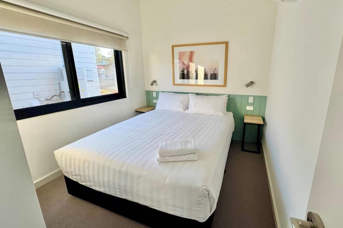 A hotel room with a bed, a window, a framed picture on the wall, and a small table.
