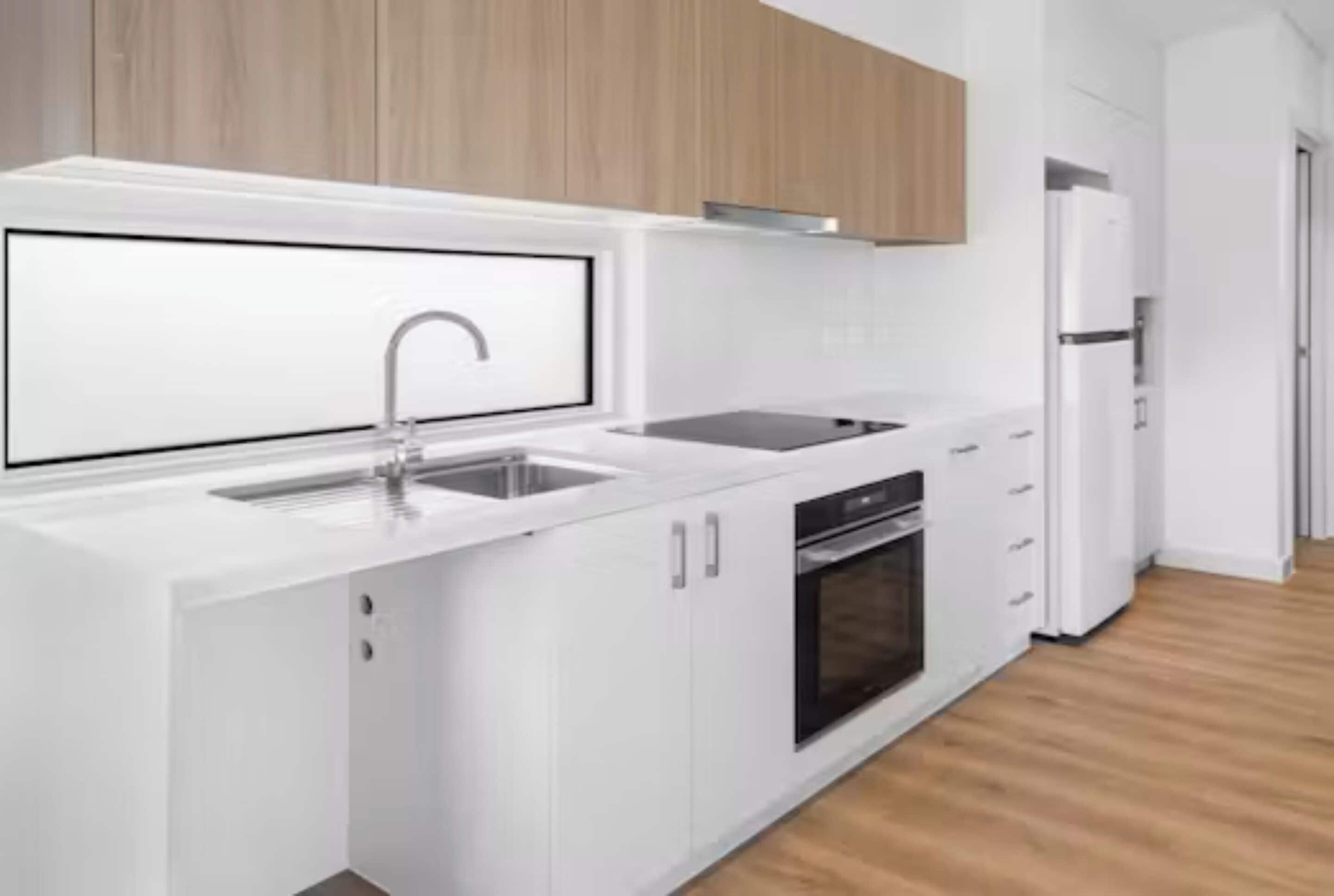 A modern kitchen with white cabinetry, a stainless steel sink, and a built-in oven.