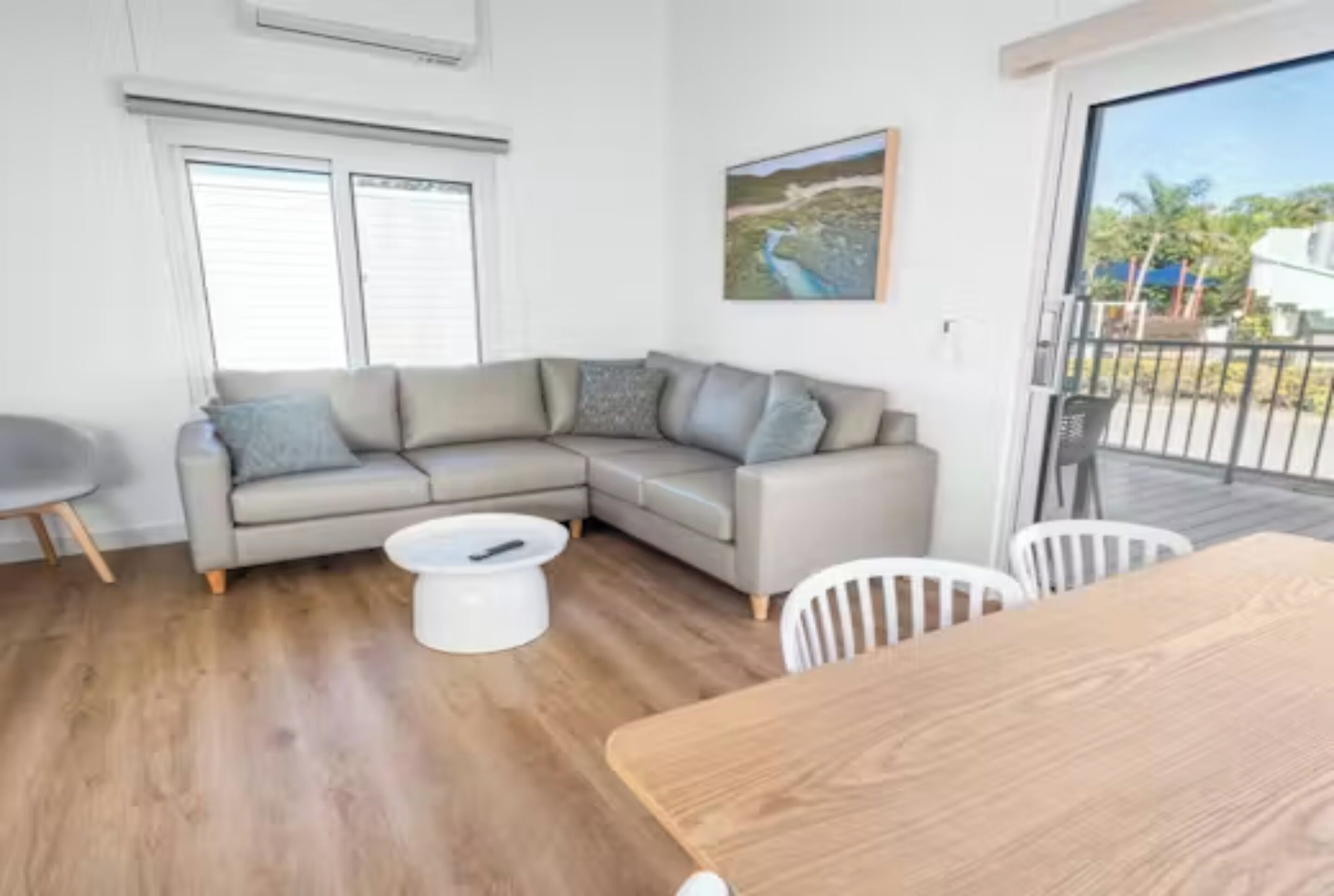 A modern living room with a grey sectional sofa, a white coffee table, and a wooden dining table.