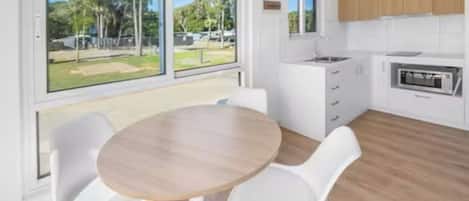 A modern kitchen with white cabinets, a built-in oven, and a large window offering a view of a grassy area.