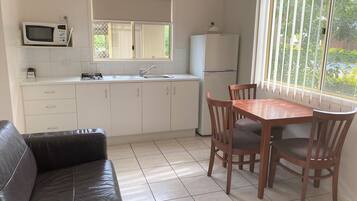 Una cocina compacta con microondas, pileta y refrigerador. Cuenta con una mesa de comedor con sillas y un sofá de cuero.