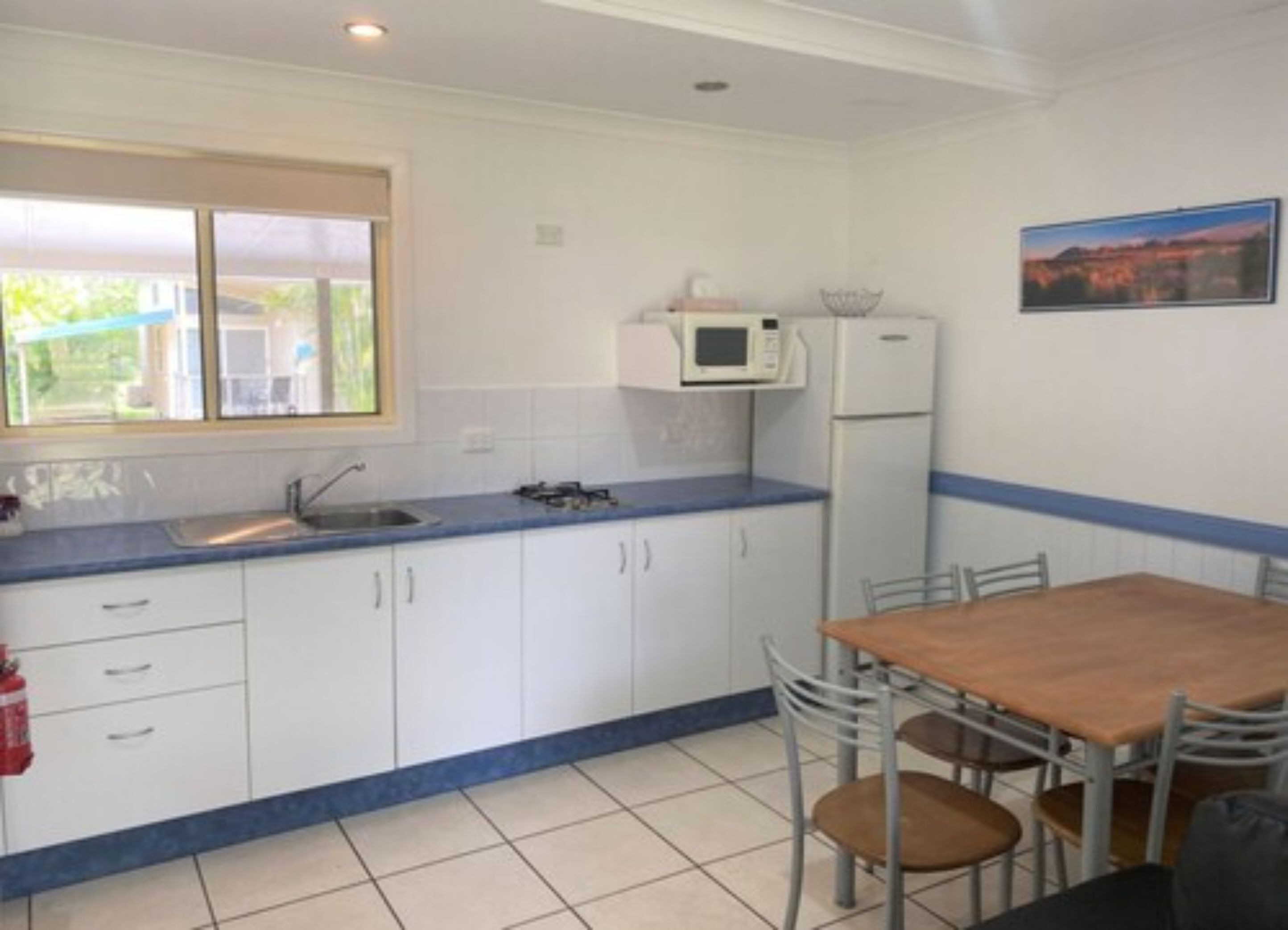 A compact kitchen with white cabinets, a blue countertop, a microwave, a refrigerator, and a dining table with chairs.
