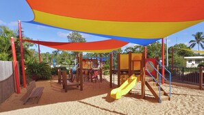 A playground with a yellow slide and climbing structures, set on sandy ground with a colorful canopy overhead. - Discovery Parks - Coolwaters Yeppoon (Kinka Beach)
