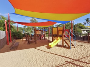 A playground with a yellow slide and climbing structures, set on sandy ground with a colorful canopy overhead. - Discovery Parks - Coolwaters Yeppoon (Kinka Beach)