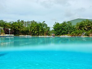 Une piscine d’eau cristalline, entourée d’une végétation luxuriante, avec un bâtiment visible au loin.