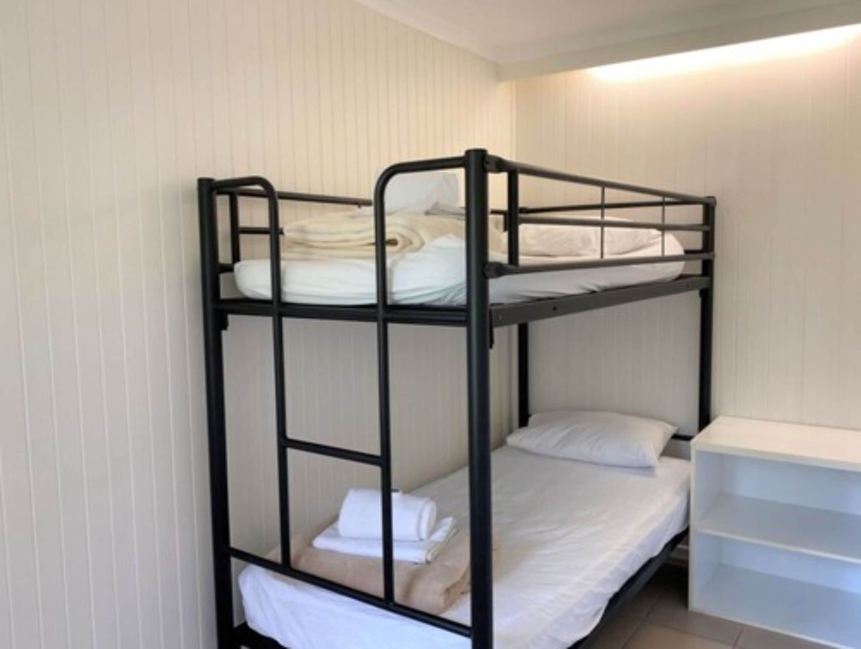 A bunk bed with white bedding and a white storage unit beside it.