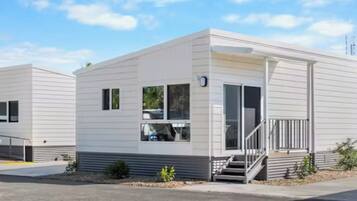 A modern, single-story mobile home with a flat roof, a front porch, and a small front yard.