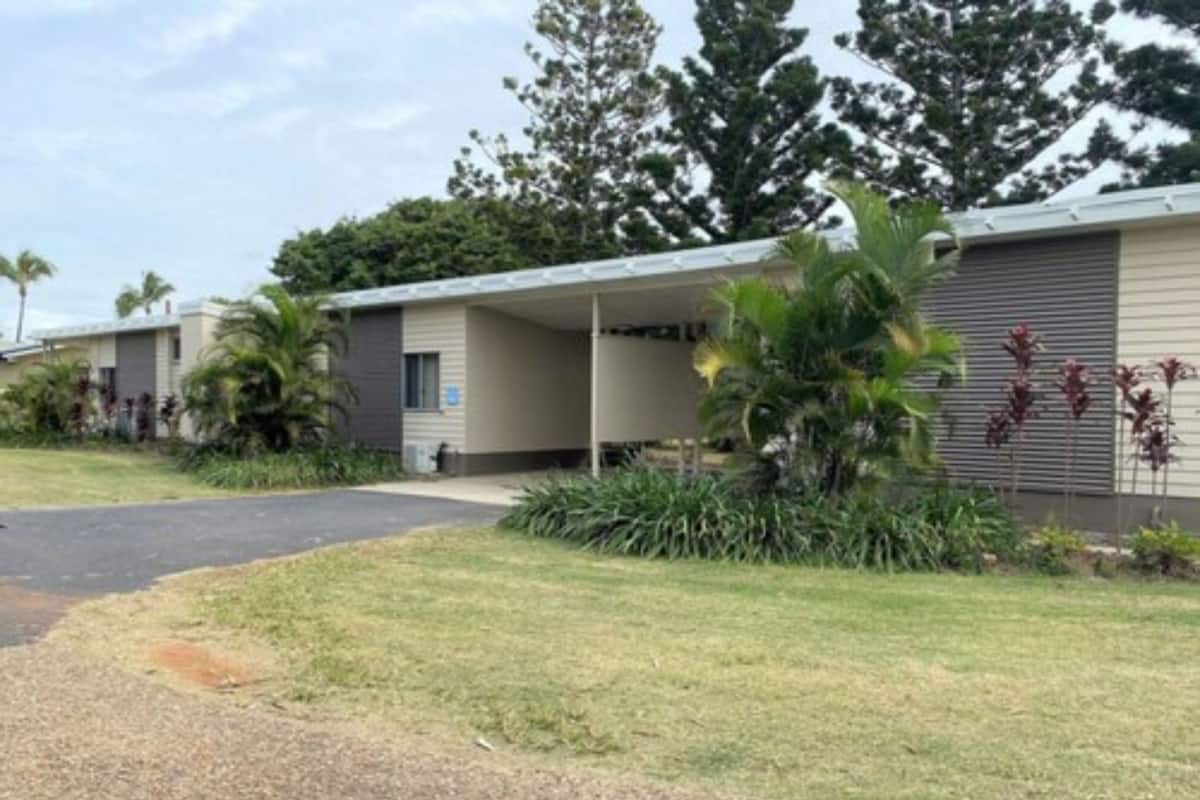 A motel with a covered parking area, a grassy lawn, and tropical plants.