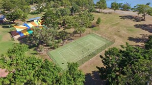 An aerial view of a park with a tennis court, picnic areas, and a lake. - Discovery Parks - Coolwaters Yeppoon (Kinka Beach)