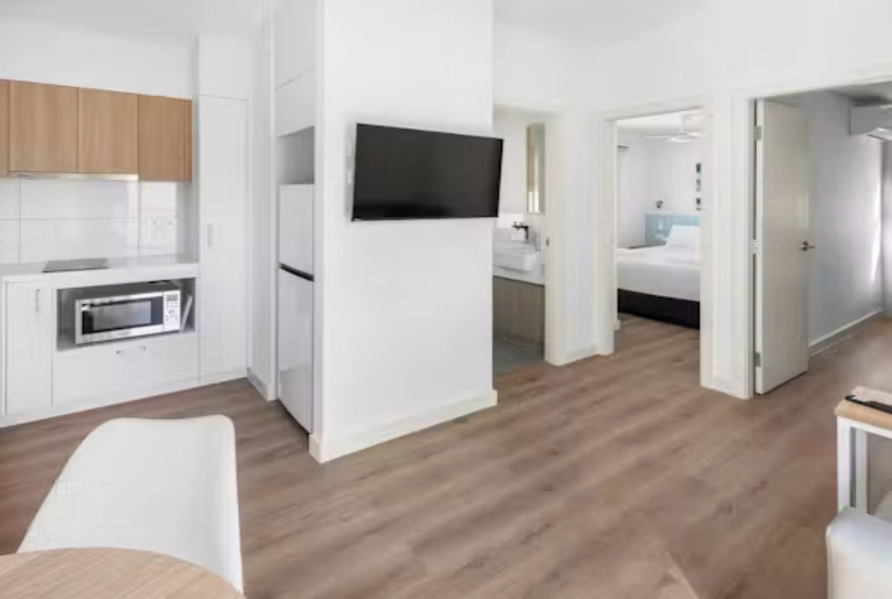 A modern kitchen with white cabinets, a built-in oven, and a flat-screen TV.