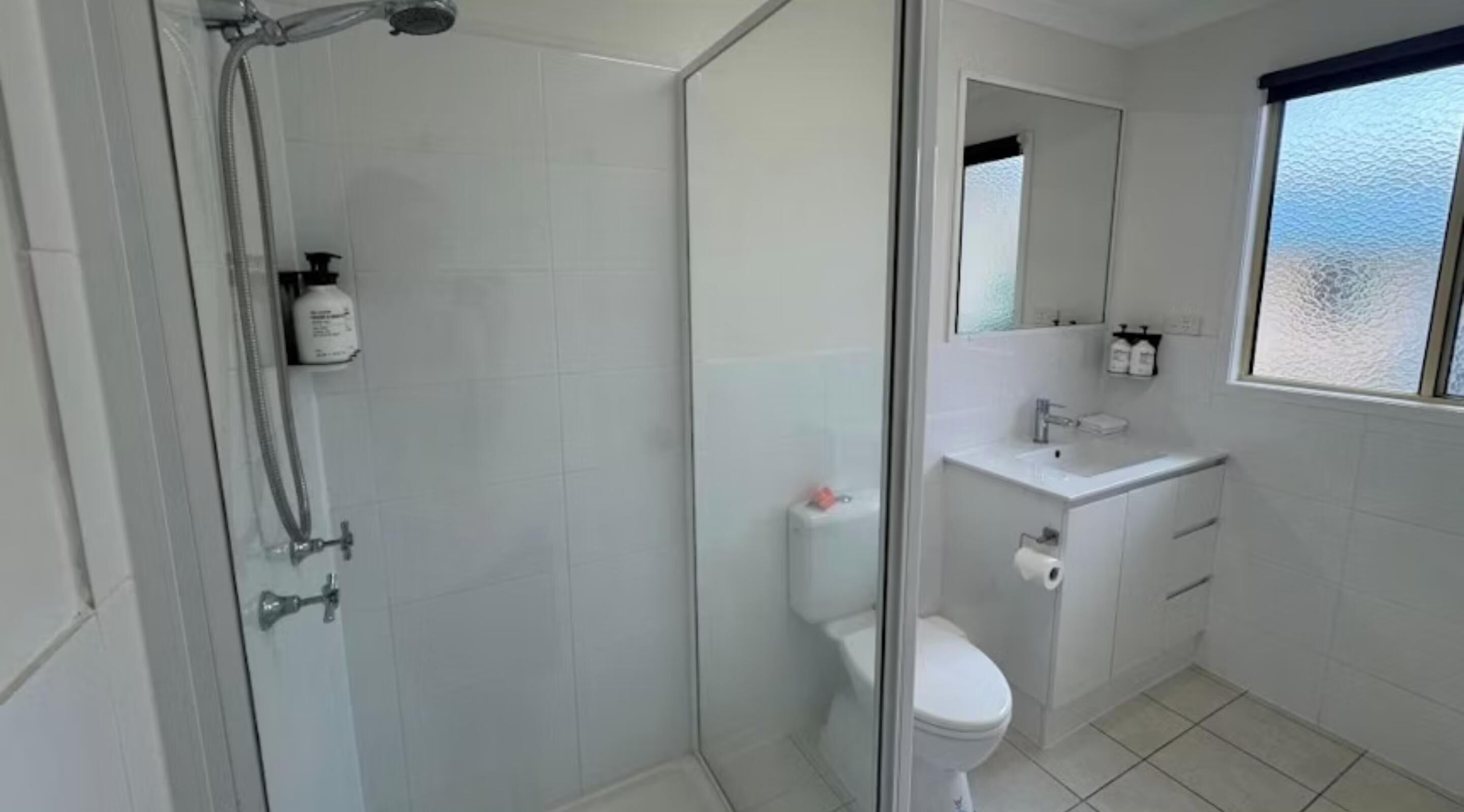 A modern bathroom with a glass shower enclosure, a toilet, a sink, and a window with a view.