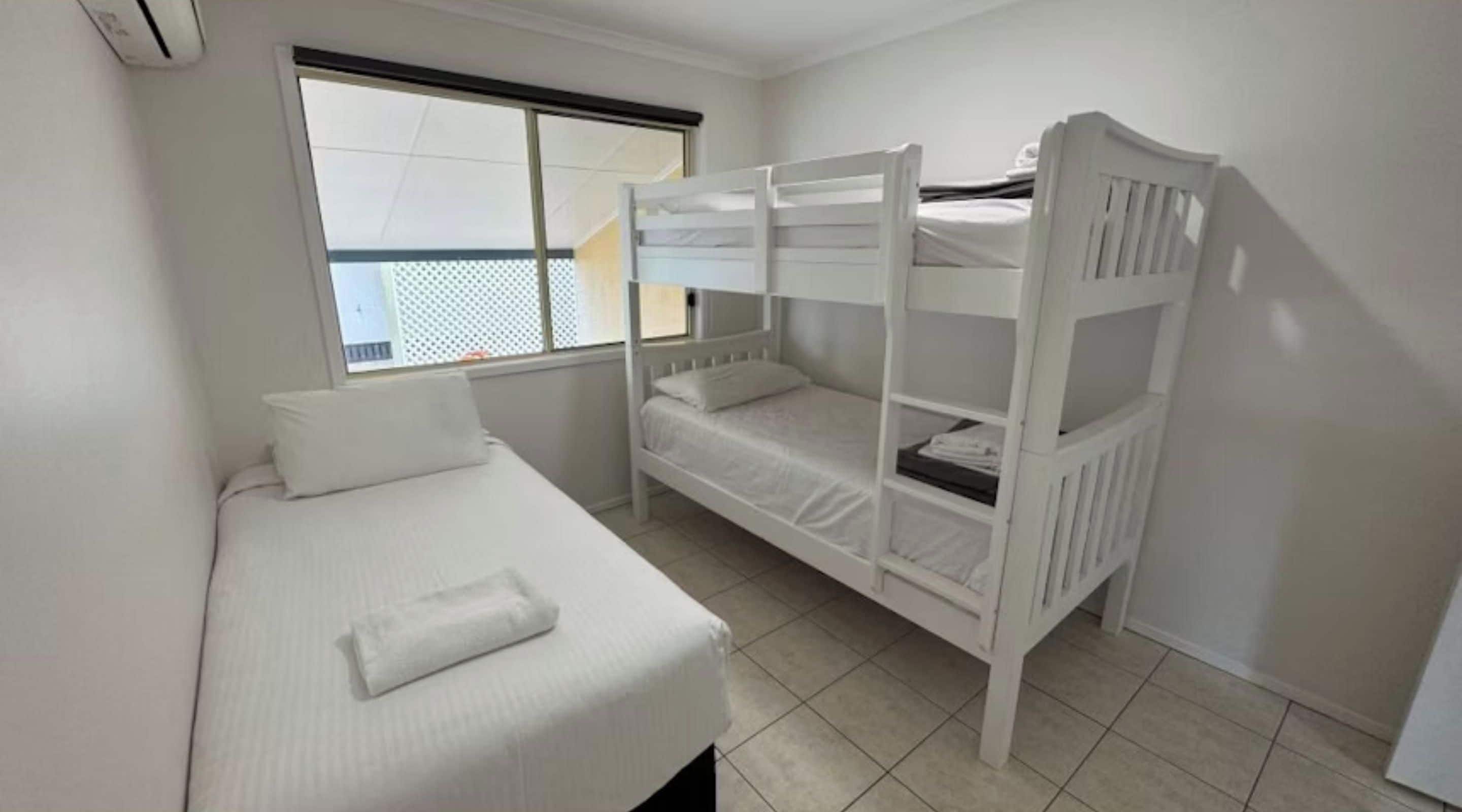A room with a bunk bed, a single bed, and a window with blinds.