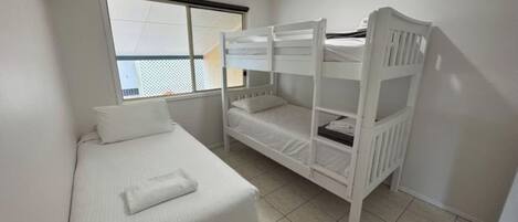 A room with a bunk bed, a single bed, and a window with blinds.