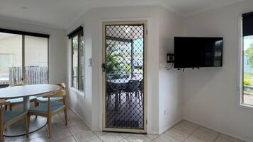 Quarto com mesa de jantar e cadeiras, televisão fixada na parede e porta que dá para o exterior.