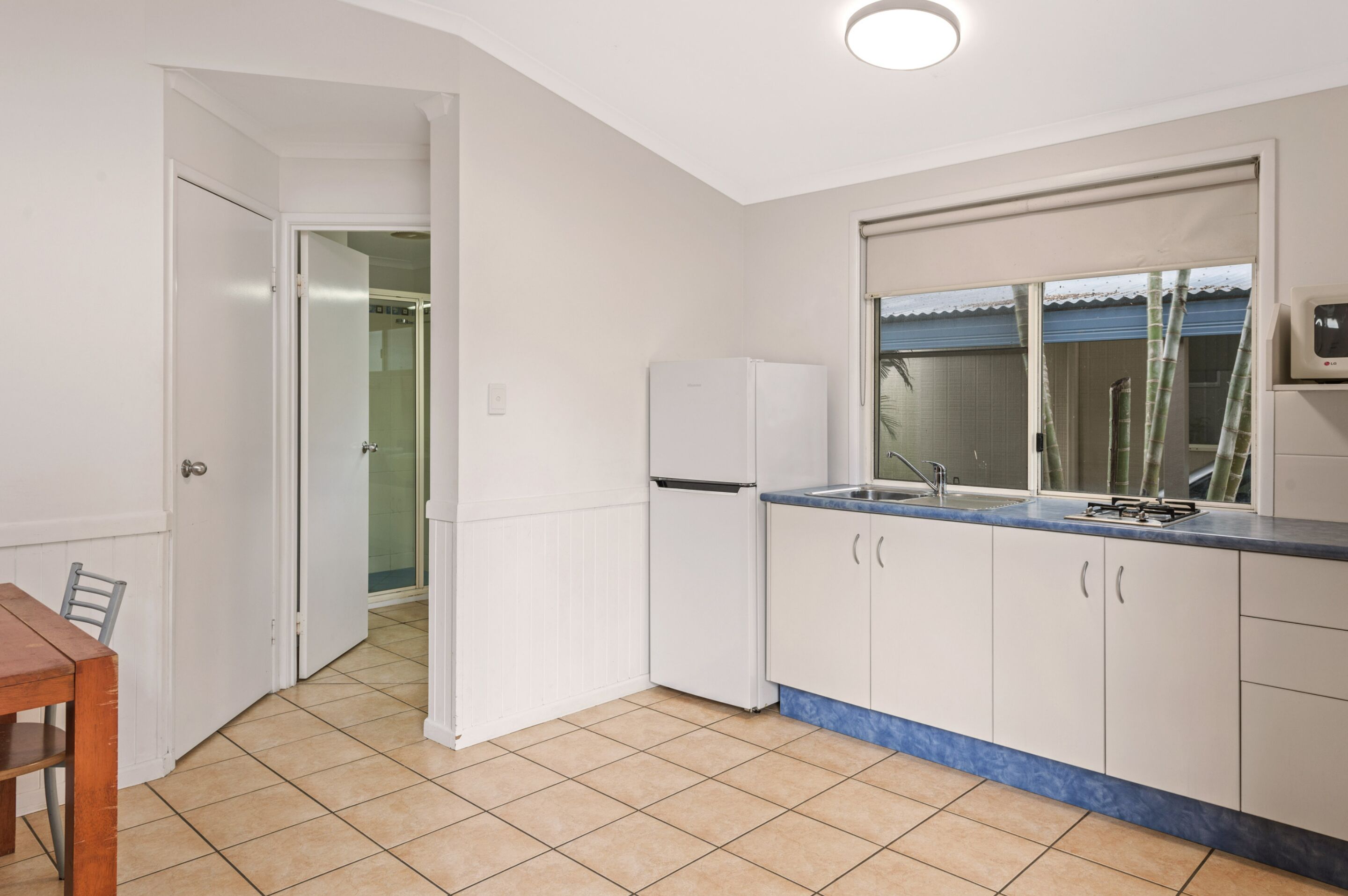 A kitchen with white cabinets, a blue countertop, and a window with bamboo blinds.