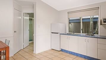 A kitchen with white cabinets, a blue countertop, and a window with bamboo blinds.