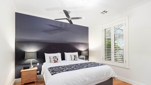 Quarto com cama, mesas de cabeceira, ventilador de teto e janela com persianas.