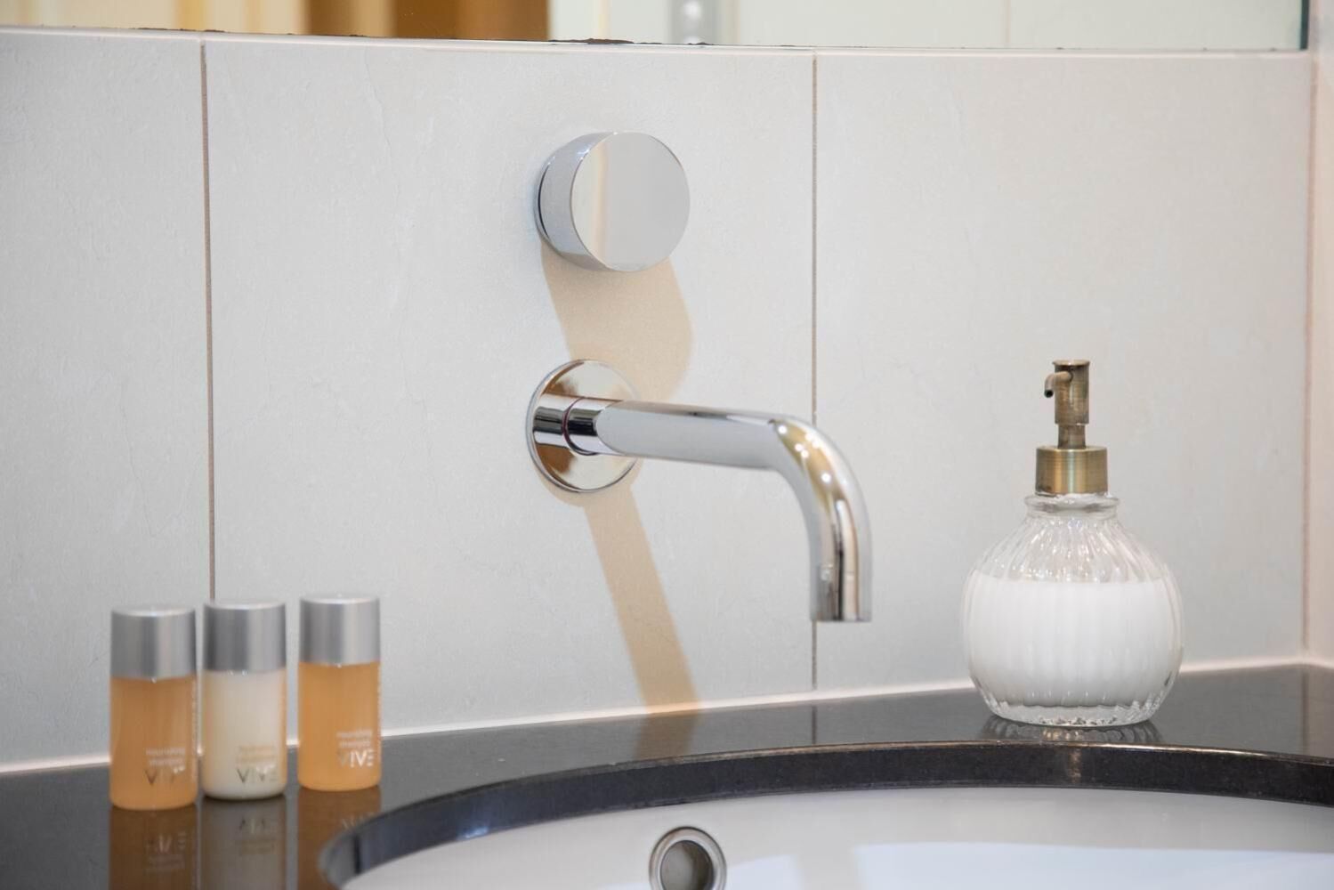 A bathroom sink with a chrome faucet and a soap dispenser. There are three bottles of lotion on the counter.