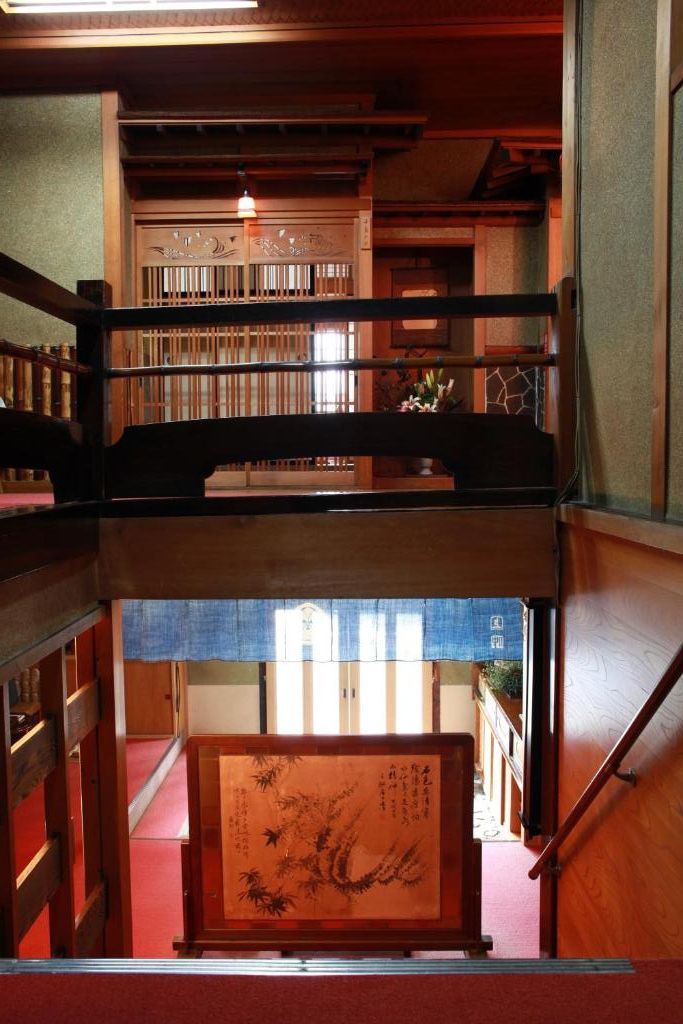 A traditional Japanese interior with a wooden staircase, tatami flooring, and a view of a building outside.