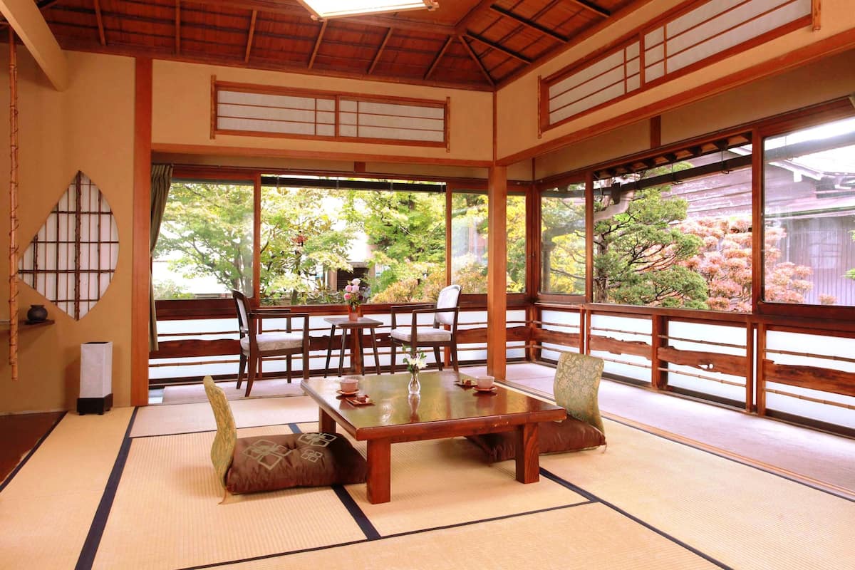 Een traditionele Japanse kamer met tatami vloerbedekking, een lage houten tafel en uitzicht op een tuin met kersenbloesems.