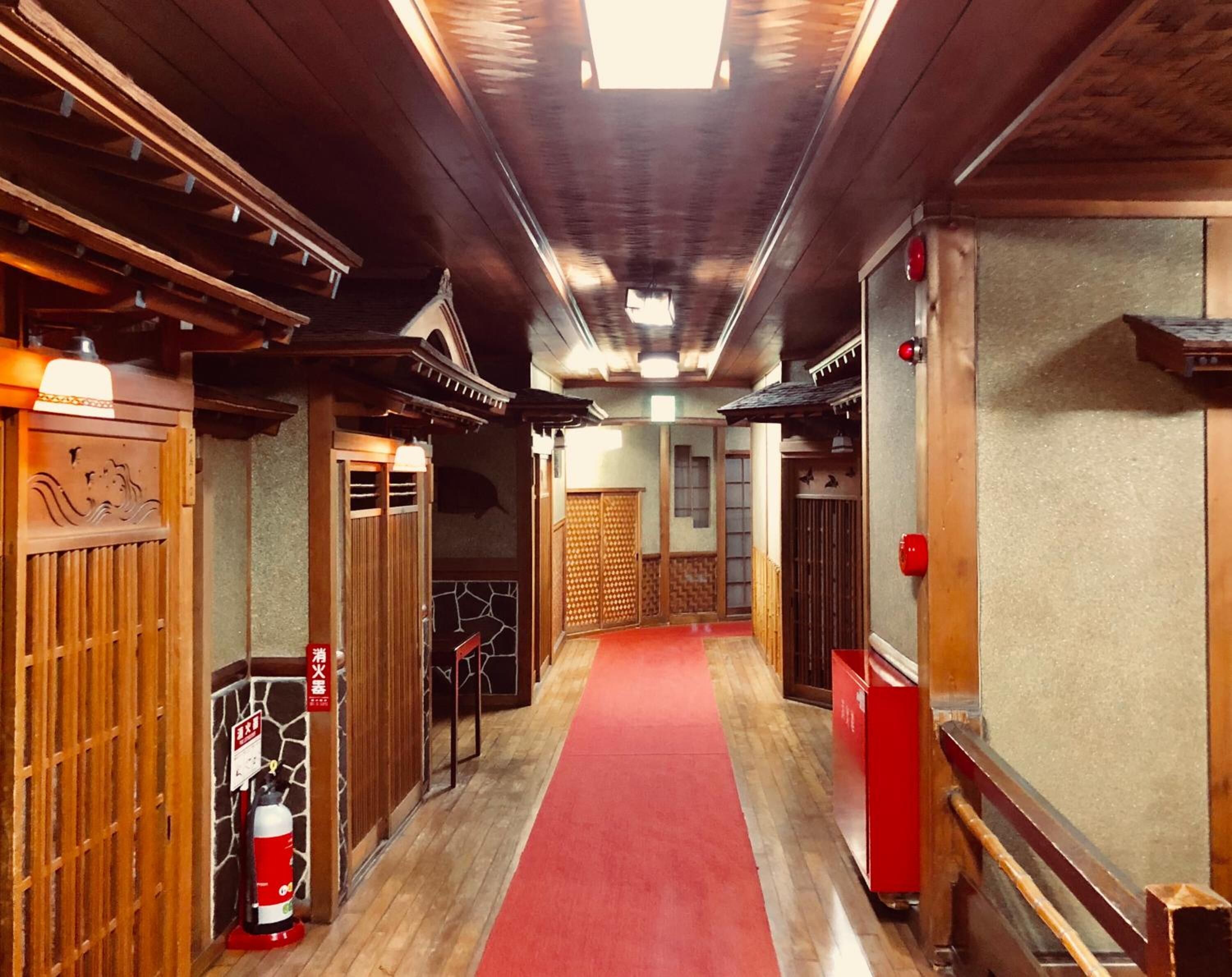 Um corredor com carpete vermelho que leva a um quarto com teto de madeira e portas japonesas tradicionais.