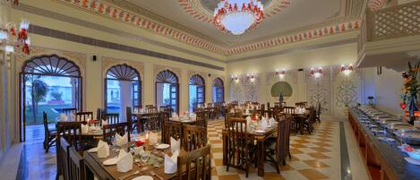 A spacious dining area with multiple tables and chairs, ornate ceiling decorations, and a buffet line.