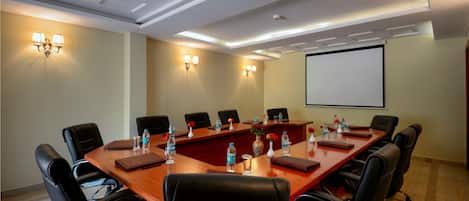 A conference room with a long wooden table, black leather chairs, and a projector screen on the wall.