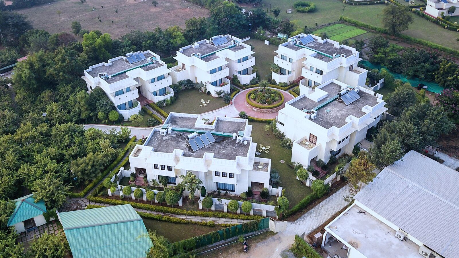 A modern residential complex with multiple white buildings, solar panels on rooftops, and well-maintained gardens.